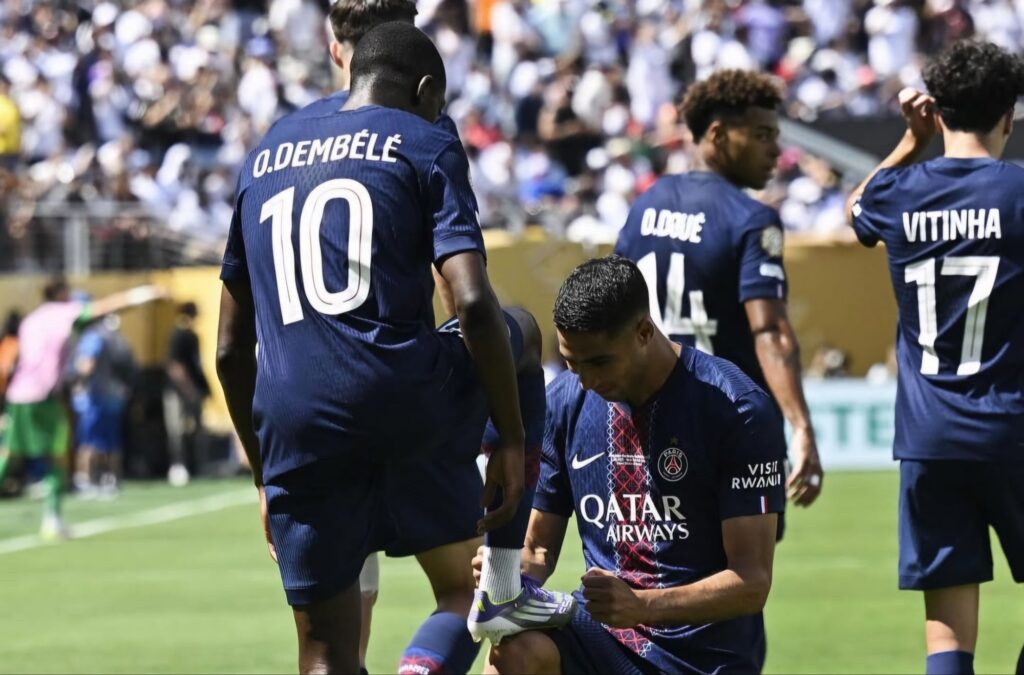 Achraf Hakimi kneels to tie Ousmane Dembélé’s boots in celebration during PSG’s Club World Cup semifinal vs Real Madrid.